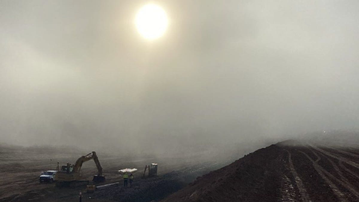 Excavators working below an embankment in early-morning fog